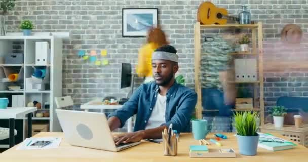 Zoom-out-Zeitraffer eines Afrikaners, der im Büro mit Laptop arbeitet — Stockvideo