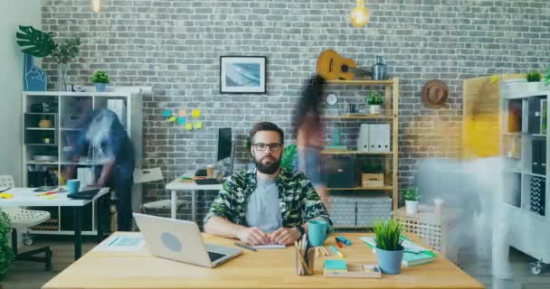 Time lapse porträtt av stilig kille sitter vid skrivbordet på kontoret tittar på kameran — Stockvideo