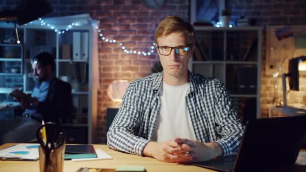 Retrato de homem sério sentado na mesa no escritório à noite olhando para a câmera — Vídeo de Stock