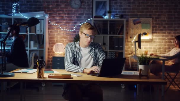 Медленное движение молодых людей, работающих в офисе поздно ночью с помощью ноутбуков — стоковое видео