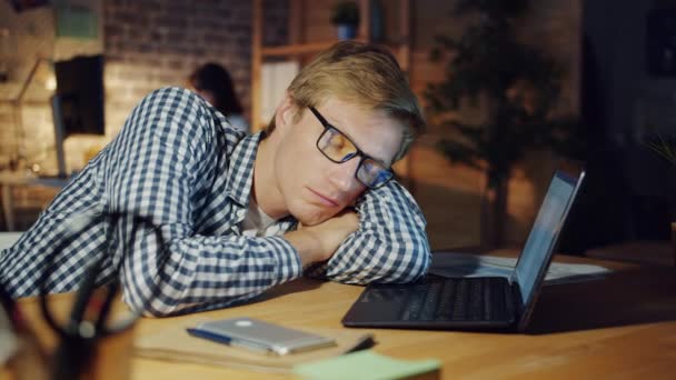 Портрет втомленого чоловіка, який спить на столі в темному офісі вночі лежить на столі — стокове відео