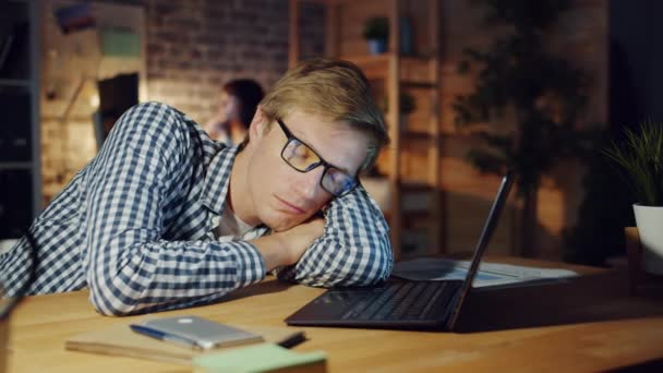 Exhausted office worker napping on desk in dark room while colleagues working — Stock Video