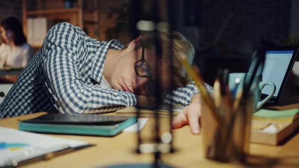 Уставший бизнесмен отдыхает в офисе, спит на столе в темной комнате ночью — стоковое видео