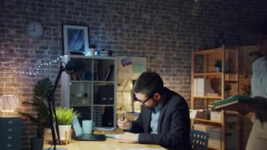 Kadın yorgun ofis çalışanına gece geç saatlerde belge getiriyor, adam mutsuz.