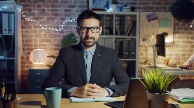 Karanlık işyerinde gülümseyen yakışıklı bir ofis çalışanının yavaş çekim portresi.