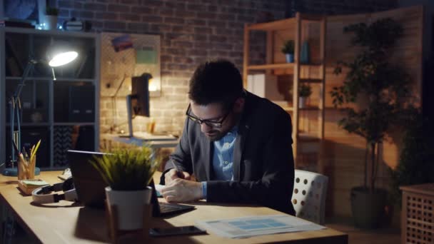 Fáradt ember dolgozik az irodában késő este, amikor a menedzser hozza a papírokat — Stock videók