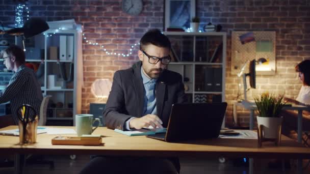 Uitgeput man voelt hoofdpijn werken in het kantoor 's nachts dan slapen op het bureau — Stockvideo