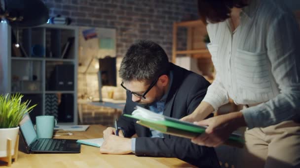 Collègue apportant des documents à un employé de bureau fatigué demandant à finir la paperasse — Video