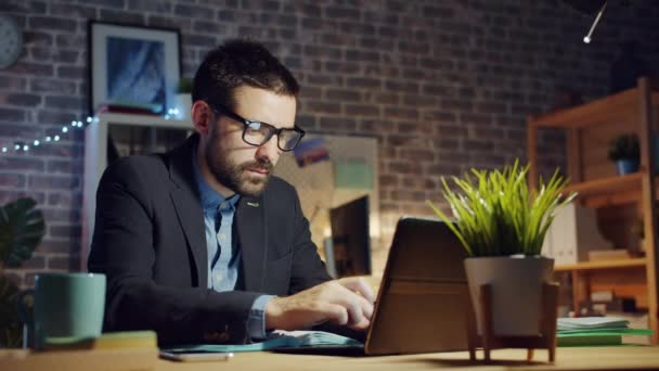 Happy guy using laptop in dark office smiling enjoying successful work at night — Stock video