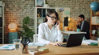 Ofiste cep telefonuyla konuşan güzel bayan ofis çalışanı gülümsüyor.