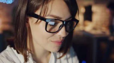 Geceleri karanlık ofiste çalışan güzel bir genç kadının yakın plan portresi.