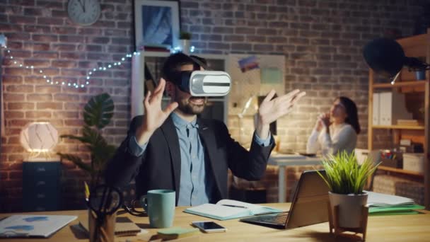 Joyful man met behulp van virtual reality bril aan het werk bewegende armen in donker kantoor — Stockvideo