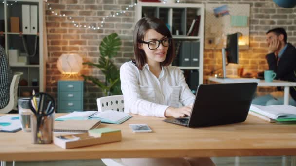 Feliz mujer de negocios está trabajando en la oficina tarde en la noche utilizando la escritura de computadoras — Vídeos de Stock