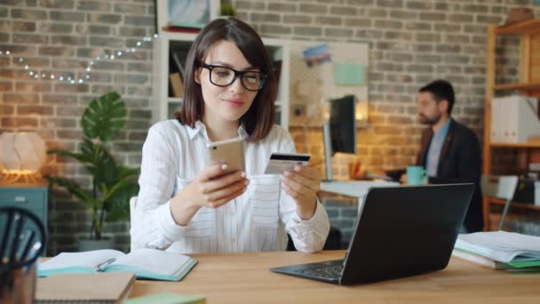 Молодая женщина делает онлайн оплату с помощью кредитной карты и смартфона на работе — стоковое видео