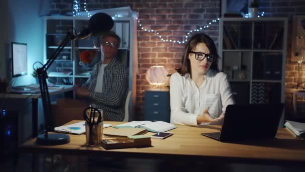 Joyful man helping female colleague with computer work talking in dark office — Stock Video