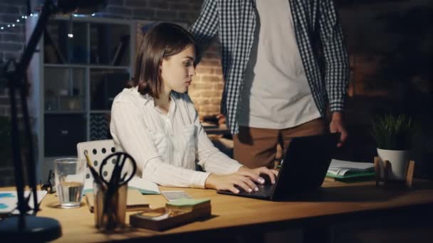 Chica agotada trabajando con el ordenador portátil cuando el gerente de traer más papeles por la noche — Vídeo de stock