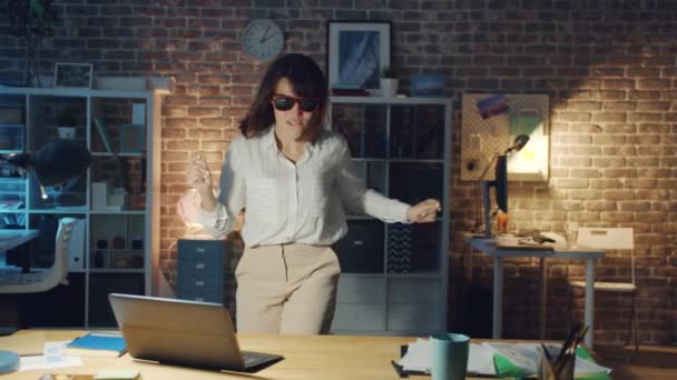 Kvinnlig kontorsarbetare i roliga glasögon som har roligt på kontoret på kvällen — Stockvideo