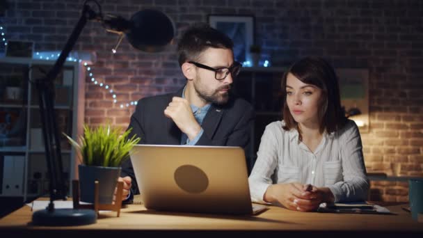 Mouvement lent de la fille et le gars à l'aide d'un ordinateur portable dans la salle de bureau la nuit parler — Video