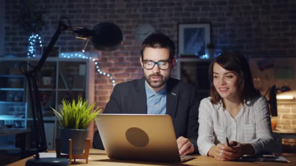Счастливые офисные работники с помощью ноутбука смеются вечером на рабочем месте — стоковое видео