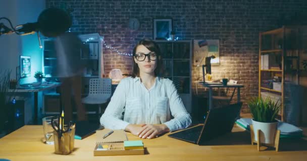 Портрет привлекательной офисной работницы, сидящей за столом ночью — стоковое видео