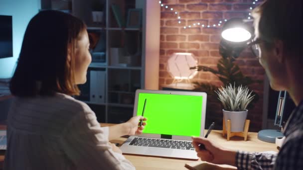 Especialistas apuntando a la pantalla del ordenador portátil de croma verde en la oficina oscura hablando — Vídeos de Stock