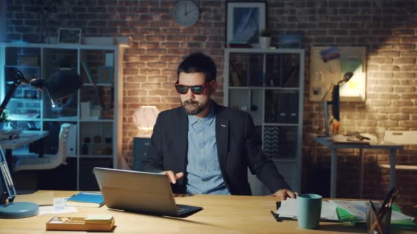 Bonito cara trabalhador de escritório girando na cadeira à noite trabalhando com laptop — Vídeo de Stock