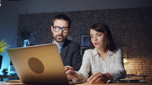 Specialisten man en vrouw op zoek naar laptop scherm praten in het kantoor 's nachts — Stockvideo