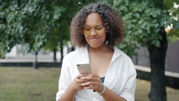 公園の屋外でスマートフォンとのコミュニケーションを楽しむアフリカ系アメリカ人女性 — ストック動画