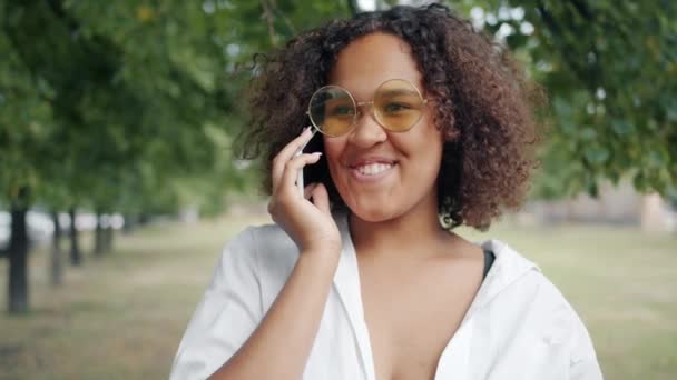 興奮したアフリカ系アメリカ人の女性が市内の公園で携帯電話で話して笑っている — ストック動画