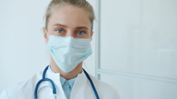 Salgın sırasında klinikte tıbbi maske takan genç sarışın kadın portresi. — Stok video