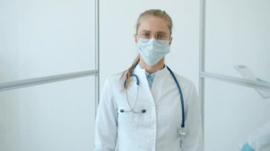 Beyaz takım elbiseli kadın doktor ve yüz maskesi beyaz arka planda yavaş hareket ediyor.