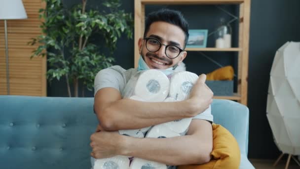 Retrato de tipo árabe feliz abrazando paquete de papel higiénico y sonriendo en casa — Vídeos de Stock