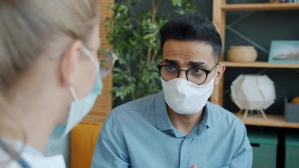 Άραβας με μάσκα προσώπου που μιλάει με γιατρό στο σπίτι ελέγχοντας τη θερμοκρασία βήχα — Αρχείο Βίντεο