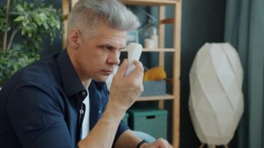 Vücut ısısını temas olmayan termometreyle ölçen ve dairede gülümseyen bir adam.