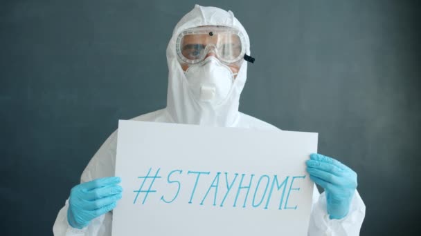 Πορτρέτο του γιατρού σε προστατευτικά ρούχα κρατώντας stayhome banner σε γκρι φόντο — Αρχείο Βίντεο