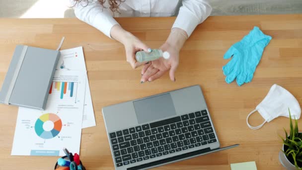 Hoge hoek van de vrouw werknemer met behulp van de hand sanitizer op de werkplek dan typen met laptop — Stockvideo