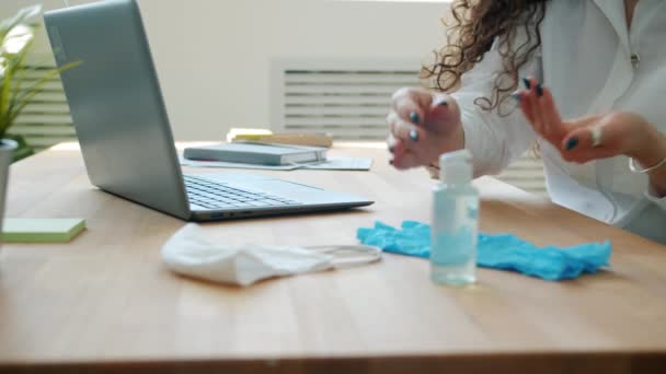 İş kadını el dezenfektanı kullanıyor, elleri dezenfekte ediyor ve ofiste bilgisayarla çalışıyor. — Stok video