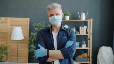 Salgın sırasında evde duran maskeli ve eldivenli olgun bir adamın portresi.