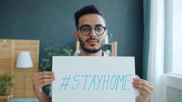 Porträtt av stilig arabisk man står hemma med stayhome affisch under covid-19 utbrott — Stockvideo