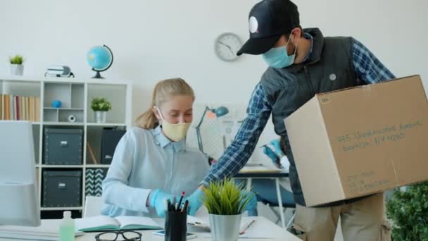 Vrouw in het gezicht masker en handschoenen krijgen pakket levering in het kantoor tijdens covid 19 pandemie — Stockvideo