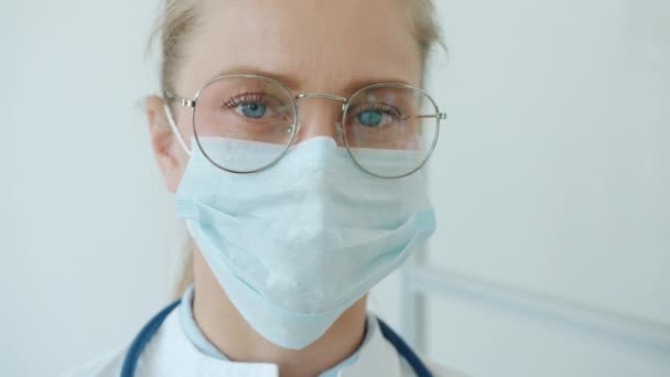 Tıbbi maske takmış genç bir kadın doktorun eldiven gözlükleriyle gözlüğe dokunuşunun yakın çekimi. — Stok video