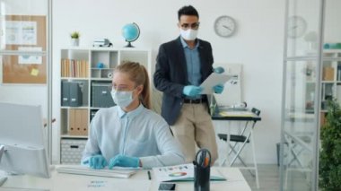 Kadın ve erkek ofis çalışanları salgın sırasında maske ve eldiven takan çizelgeler ve bilgisayarlarla çalışıyorlar.