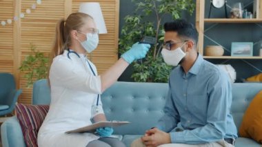 Dairesinde kızılötesi termometreyle hasta sıcaklığını ölçen kadın doktor.