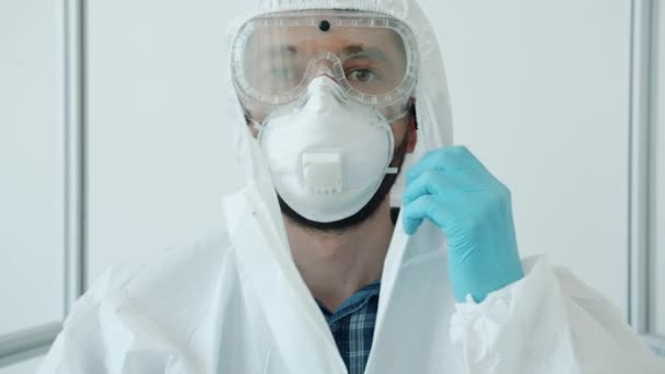 Медленное движение привлекательного молодого человека врач снимает защитный медицинский костюм в клинике и улыбается — стоковое видео