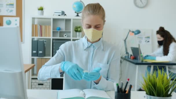 Jovem mulher em máscara facial e luvas lavar as mãos com desinfetante no escritório — Vídeo de Stock