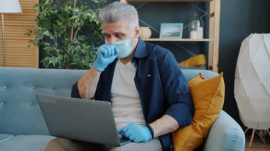 Maskeli ve eldivenli bir adamın laptopunu kullanarak doktorla konuşması ağır çekim.