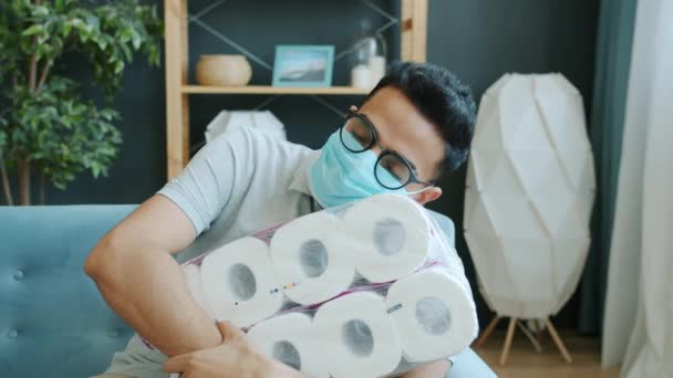 Portrét arabského muže v lékařské masce držícího doma na gauči balíček toaletního papíru — Stock video