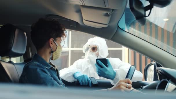 Muž v lékařském obleku měření tělesné teploty ženy řidiče v autě venku během covid-19 pandemie — Stock video
