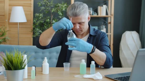 Porträt eines gutaussehenden Mannes, der in seiner Wohnung ein selbstgemachtes Händedesinfektionsmittel herstellt und dabei in die Kamera schaut — Stockvideo