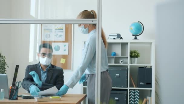 Ragazza e ragazzo colleghi in maschere facciali e guanti discutendo di lavoro comunicare in ufficio — Video Stock